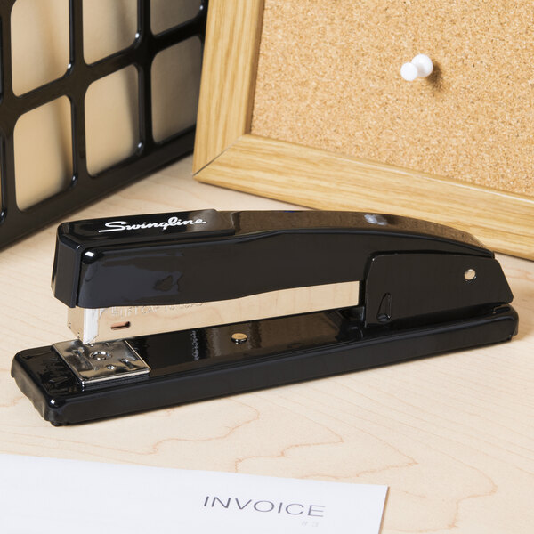 A close-up of a black Swingline desk stapler on a table with paper and a receipt.