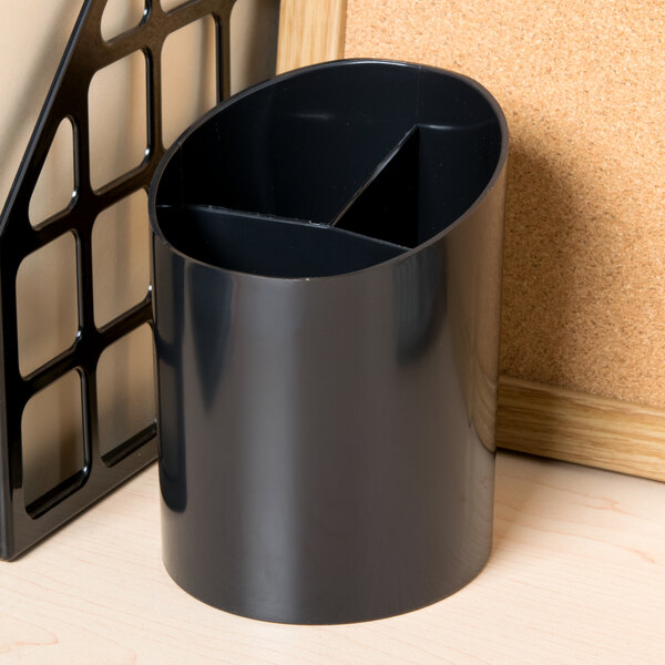 A black Universal black plastic pencil cup on a counter next to a cork board.