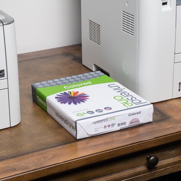 A white box of Universal Orchid Color Copy Paper on a desk next to a green and white box.