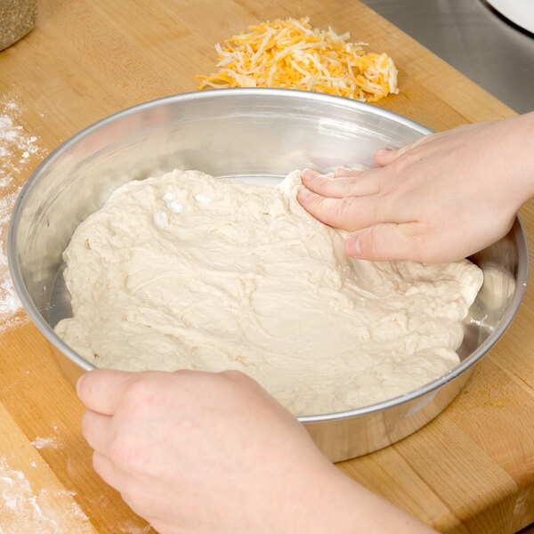 A person's hand kneading dough in a bowl on a counter.