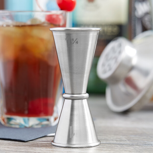 An American Metalcraft stainless steel Japanese style jigger on a table with a cocktail.