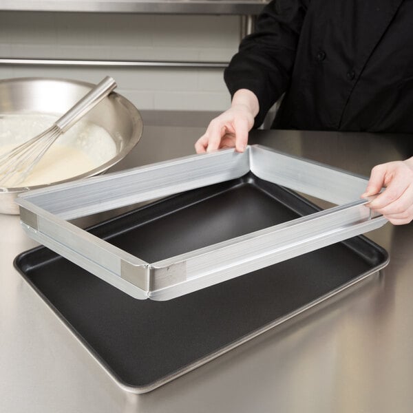 A woman using a Baker's Mark half-size sheet pan extender to hold a cake on a baking tray.