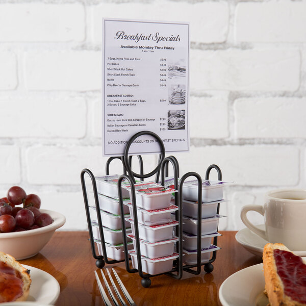 A Tablecraft black wire jelly packet rack on a table with trays of food.