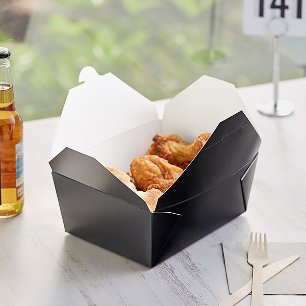 A black folded paper take-out box with fried chicken inside on a table.