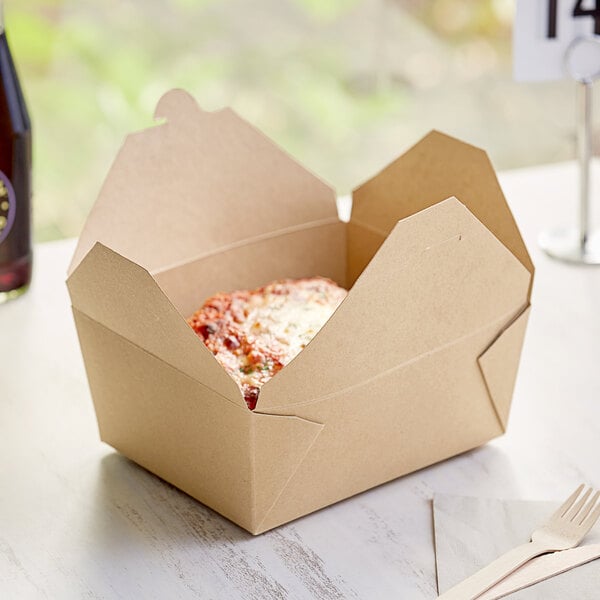 A Kraft paper take-out box with food inside and a wooden fork on a white surface.