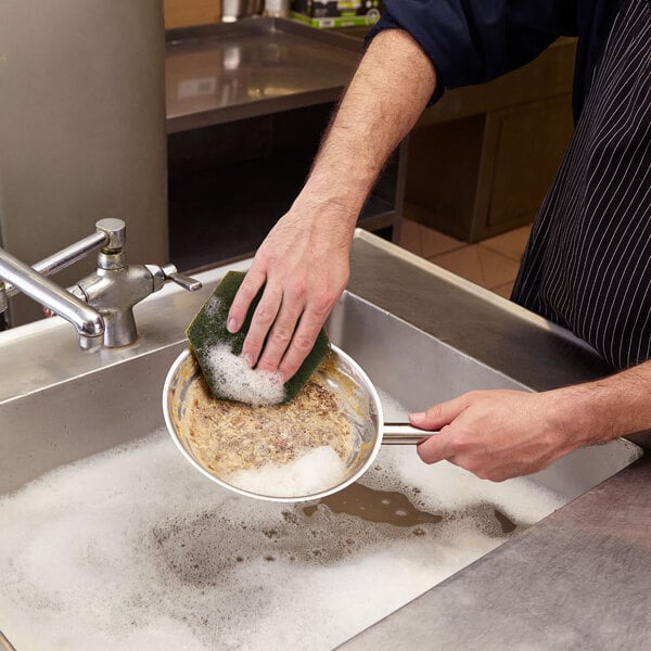 A person using a Scotch-Brite Dual Purpose Scour Pad to wash a pan in a sink.