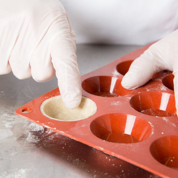 A person wearing gloves putting dough into a Matfer orange silicone tartlet mold.