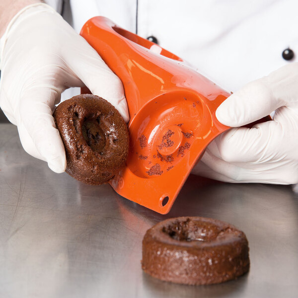 A person in gloves using a Matfer Bourgeat orange silicone savarin mold to make chocolate doughnuts.