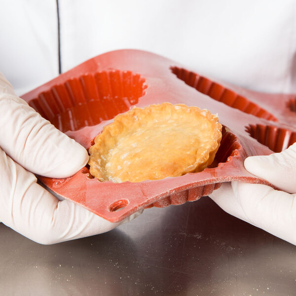 A gloved hand placing a pastry in a Matfer Bourgeat orange silicone fluted tart mold.