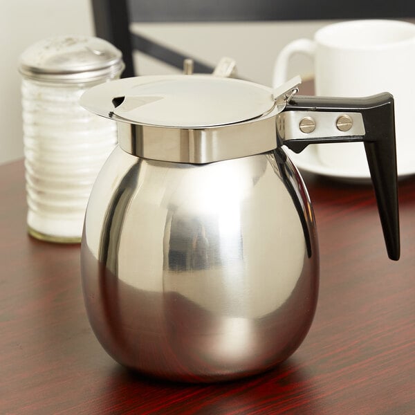 A Thunder Group stainless steel coffee decanter with a black handle on a table.