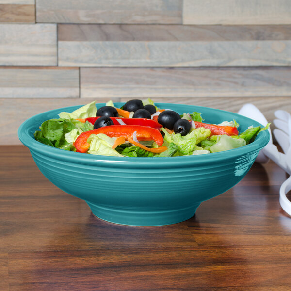 A Fiesta china pedestal serving bowl filled with salad and vegetables on a table.