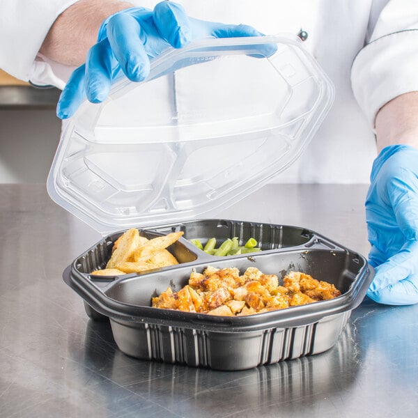 A person in blue gloves holding a Solo black plastic container with food.