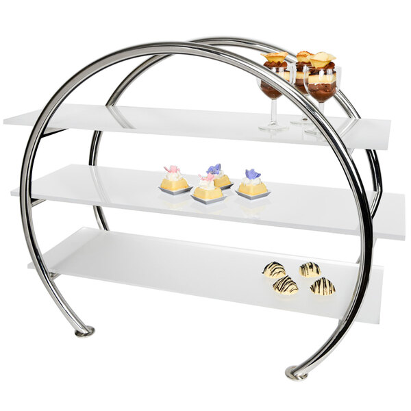 A stainless steel circular display stand with three acrylic shelves holding desserts.