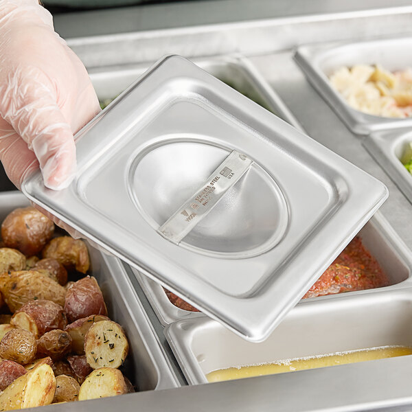 A person holding a Vigor stainless steel steam table pan cover over a tray of food.