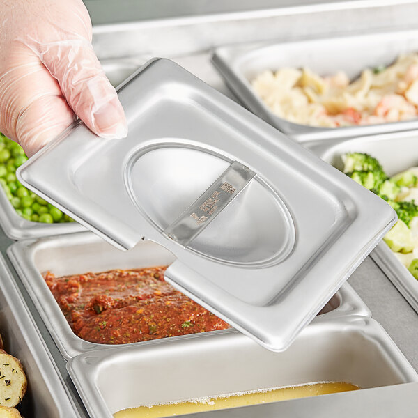 A hand holding a Vigor stainless steel slotted tray of food.