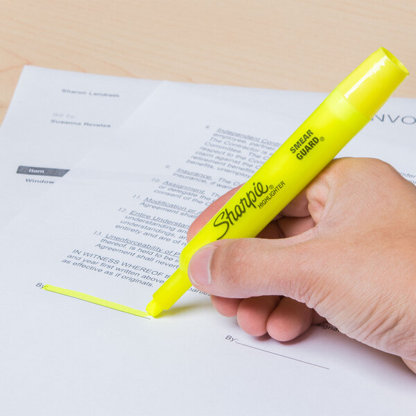 A hand using a Sharpie yellow highlighter to mark a paper.