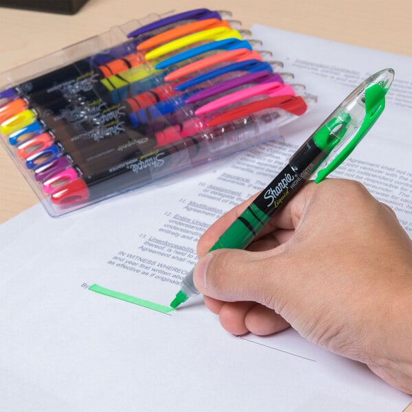 A person holding a green Sharpie highlighter over a piece of paper.