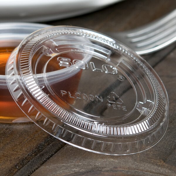 A Solo clear plastic souffle lid on a plastic container on a table.