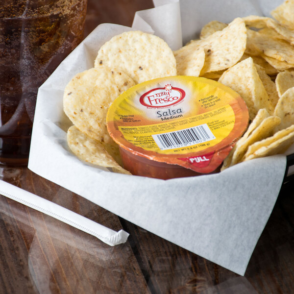 A bowl of tortilla chips with a container of Muy Fresco Medium Salsa on a table.