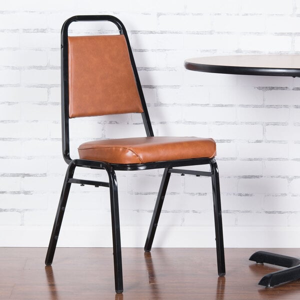 A Lancaster Table & Seating brown stackable chair with a 2" padded seat next to a table.