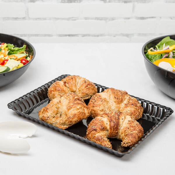 A Fineline black plastic rectangular tray with a salad and croissants on a table.