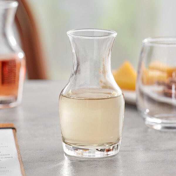 An Acopa glass carafe of liquid sits on a table next to a plate.