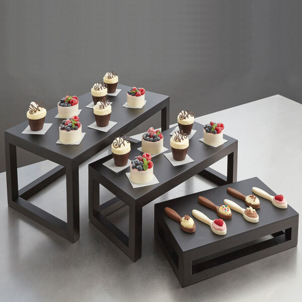 A table with American Metalcraft black wood risers holding small cupcakes.
