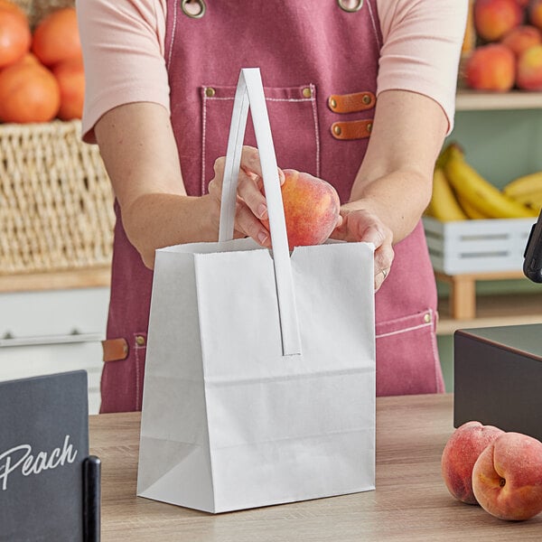 A woman in a pink apron holding a white Choice market stand bag with a peach inside.