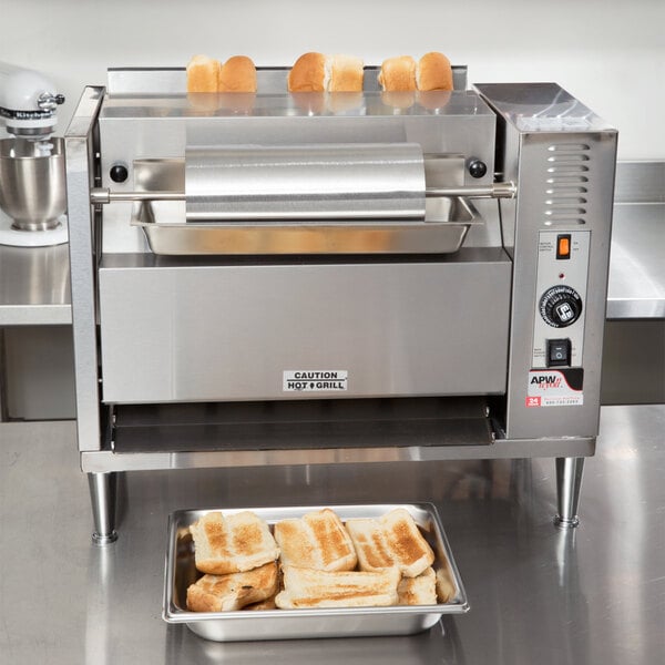 An APW Wyott Vertical Conveyor Bun Grill Toaster with bread toasting on a metal bar.