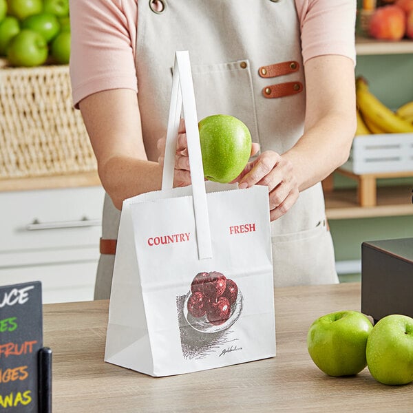 A woman holding a green apple in a white "Country Fresh" paper bag.