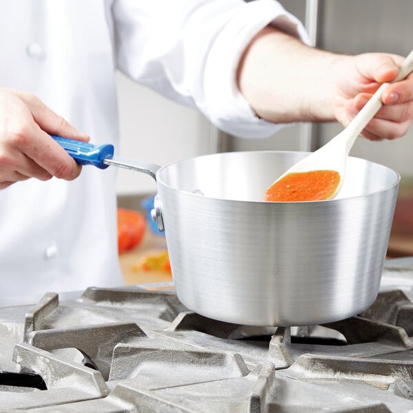 A person stirring sauce in a Vollrath Wear-Ever sauce pan.