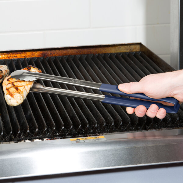 A person using Vollrath Jacob's Pride stainless steel tongs with a blue Kool Touch handle to cook on a grill.