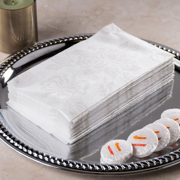A stack of Hoffmaster Linen-Like paper guest towels on a silver tray with white napkins and candies.