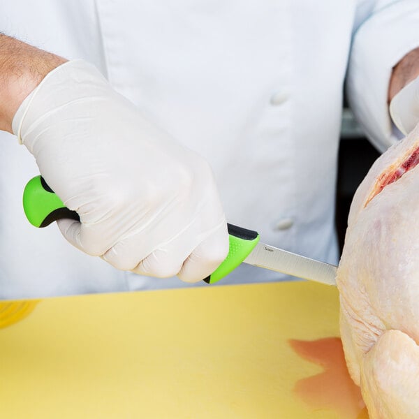 A person in white gloves using a Mercer Culinary Millennia Colors® boning knife with a green handle to cut chicken.