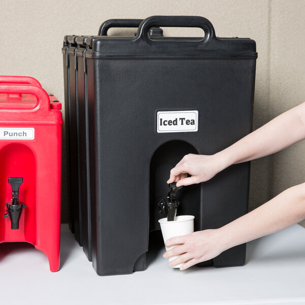 A person pouring a drink from a black Cambro insulated beverage dispenser.