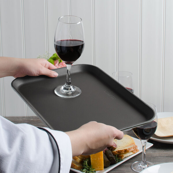 A person holding a Cambro non-skid serving tray with a glass of wine.