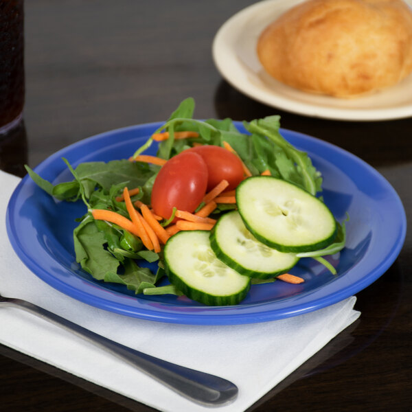 A Carlisle ocean blue melamine plate with a salad and a fork on a table with more salad plates.