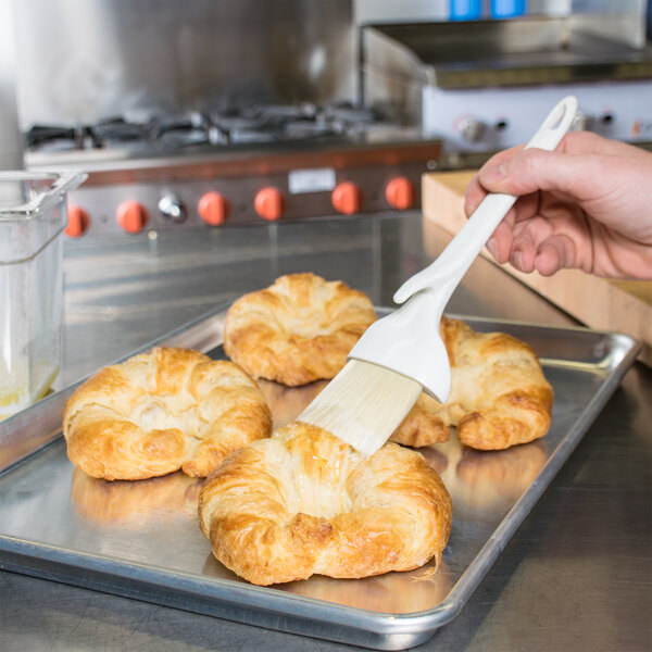 A close up of a Winco Boar Bristle Pastry Brush being used to brush butter on a croissant.
