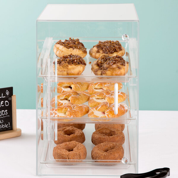 A Cal-Mil three tier display case filled with pastries and donuts on a bakery counter.