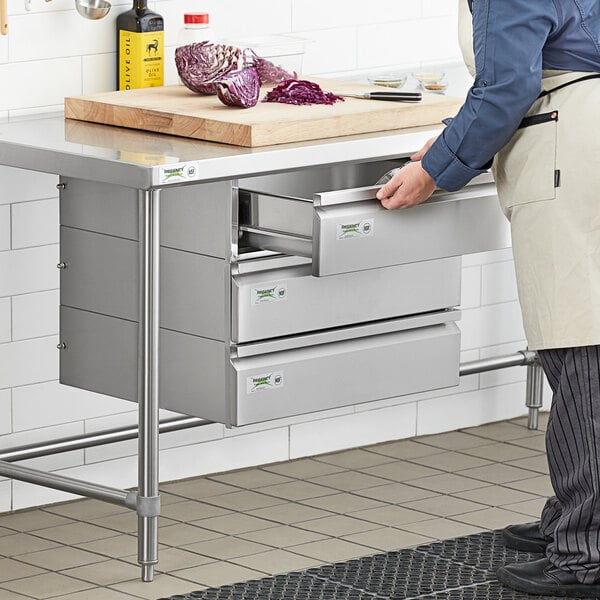 A man in a white apron opening a stainless steel drawer on a counter.