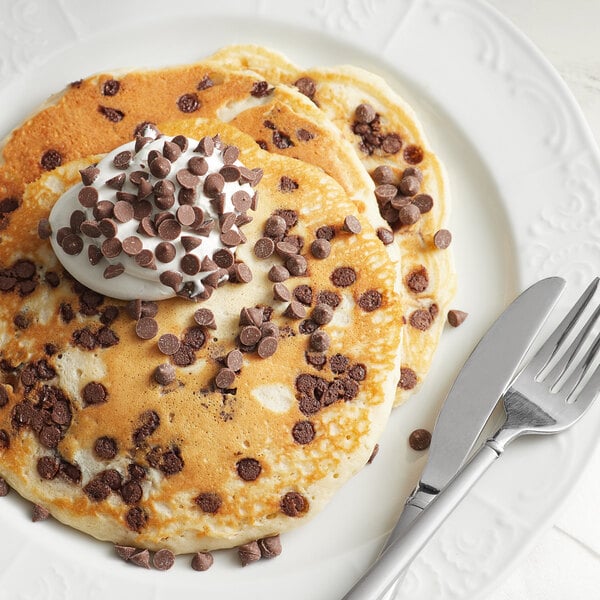 A plate of pancakes with chocolate chips and whipped cream.