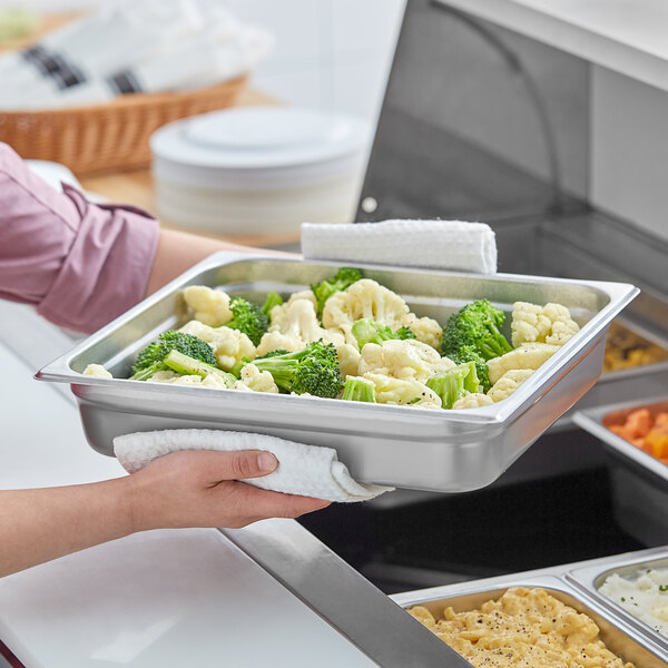 A person holding a Choice stainless steel steam table pan filled with broccoli and cauliflower.