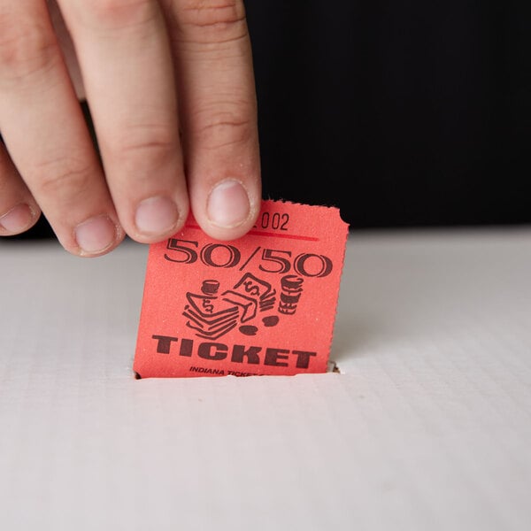 A person's fingers putting a red 50/50 marquee raffle ticket into a white box.