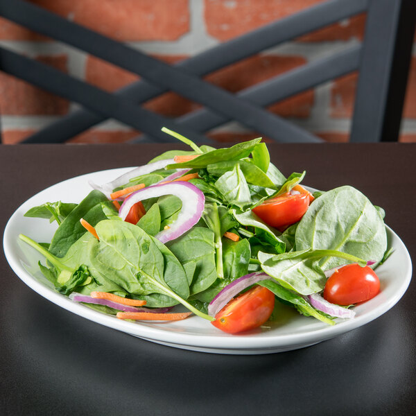 A Tuxton bright white oval china platter with a salad of spinach and tomatoes.