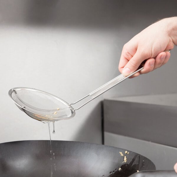 A hand using a 5 1/2" stainless steel strainer over a pan.