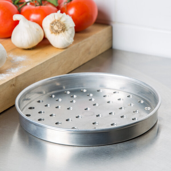 An American Metalcraft heavy weight aluminum perforated pizza pan with tomatoes and garlic on a white background.