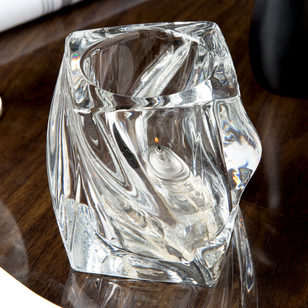 A Sterno clear glass twist candle holder on a table with a lit candle inside.