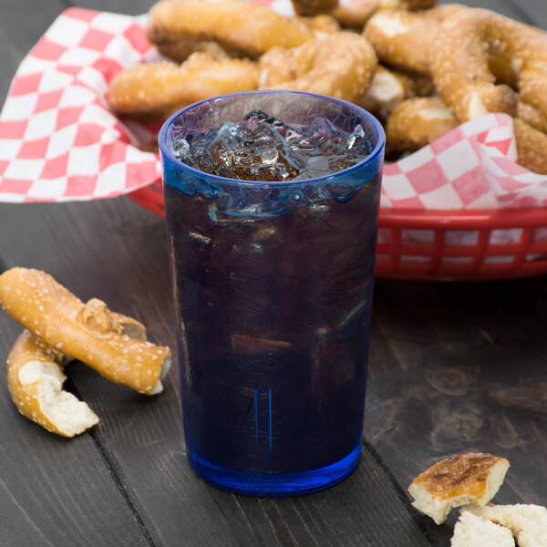 A Cambro Sapphire Blue plastic tumbler filled with soda on a table with a basket of pretzels.