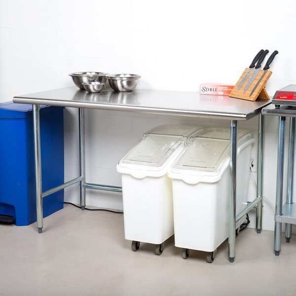 A stainless steel Advance Tabco work table with white containers on it.