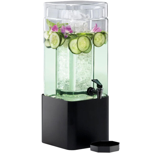 A Cal-Mil square glass beverage dispenser with a black metal base filled with water, cucumbers, and ice.
